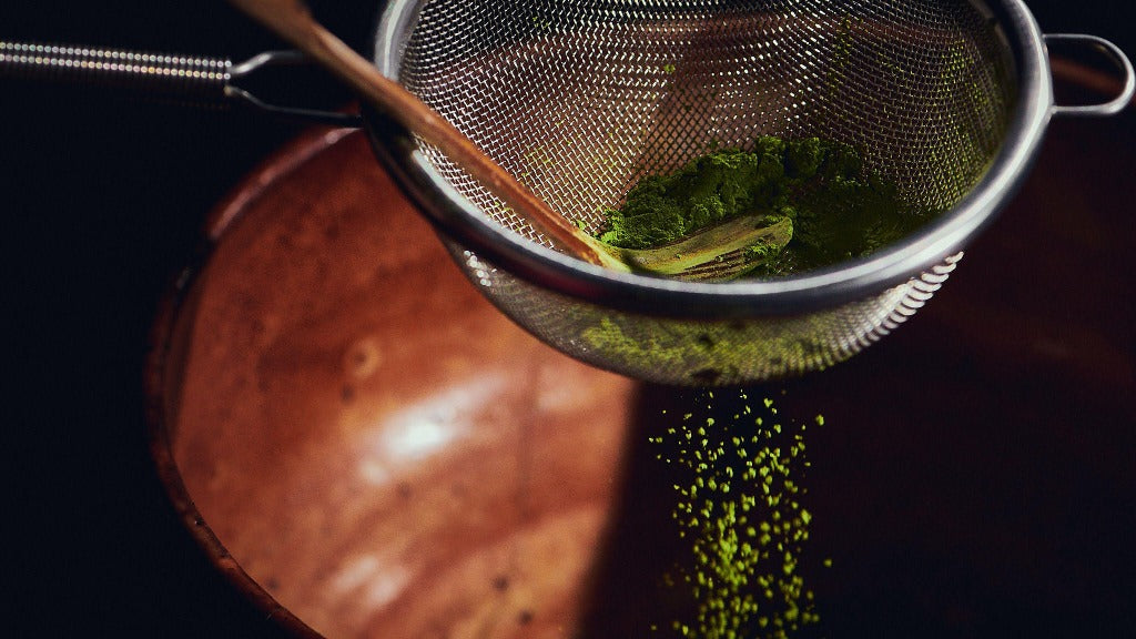 Matcha powder falling through a sifter into a copper bowl